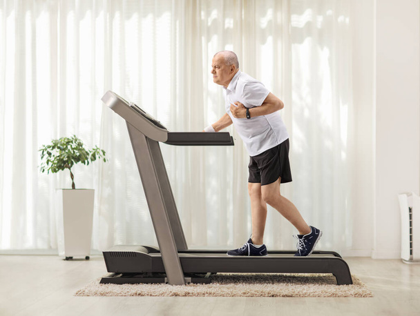 Full length profile shot of a mature man walking on a treadmill and having a heart attack at home - Zdjęcie, obraz