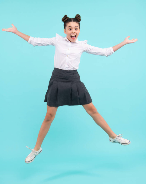Excited face. Amazed expression, cheerful and glad. Full length cheerful teenager kid jump enjoy rejoice win isolated on blue background. Small child girl in summer dress jumping - Zdjęcie, obraz