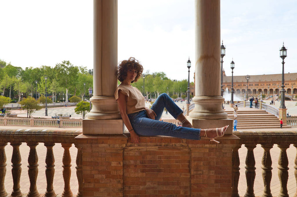 Piękna kobieta zwiedza Sewillę, kobieta siedzi między dwiema kolumnami na największym i najsłynniejszym placu w Sewilli. Kobieta jest szczęśliwa. Pojęcie urlopu i podróży. - Zdjęcie, obraz