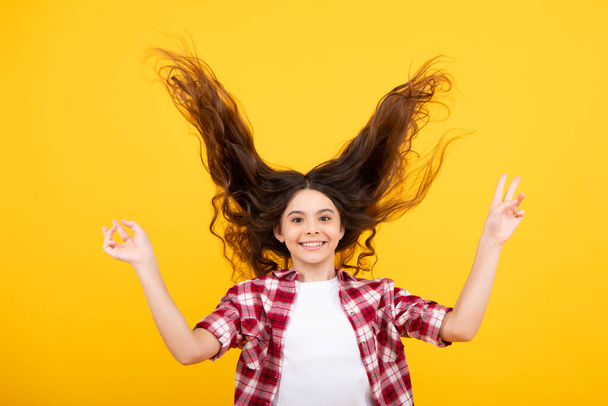 Teenager-Porträt mit verrücktem Bewegungshaar. Junges Teenager-Kind mit wallenden Haaren. Brünettes Teenager-Mädchen flatterndes Haar in Bewegung, isoliert auf gelbem Hintergrund - Foto, Bild