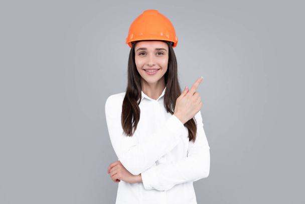 Woman in helmet pointing on copy space on gray background. Architect businesswoman in helmet, young caucasian female in work as constructor engineer - Photo, Image