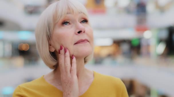 Female portrait mature caucasian woman tourist keeps hand on chin carefully examines surroundings surprised elegant lady stands in new huge mall looks around in amazement amazed by beauty of building - Footage, Video