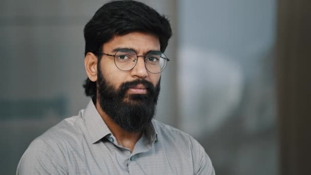 Arab hispán jóképű szakállas férfi magabiztos barna srác szemüveg fordul fej kamera pozitív arckifejezés indiai fiatal intelligens üzletember vezető munkás férfi alapító állni beltérben - Felvétel, videó