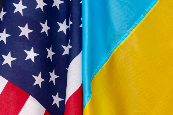 Die Flagge Amerikas und die Flagge der Ukraine werden in Großaufnahme zusammengefügt, die Flaggen gebeugt und geschwenkt. Konzept: Gemeinsame Besprechung, Leih- und Leasinghilfe. - Foto, Bild