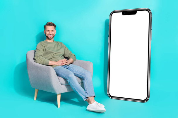 Photo of cheerful relaxed confident man sit armchair placard empty space wear pullover isolated blue color background. - Φωτογραφία, εικόνα