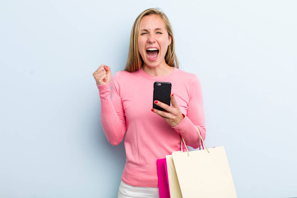 young adult blonde woman feeling shocked,laughing and celebrating success. shopping bags concept - Photo, image