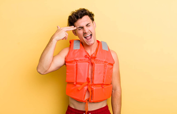 young handsome guy looking unhappy and stressed, suicide gesture making gun sign. life jacket and boat concept - Foto, afbeelding