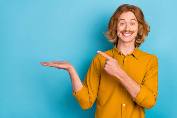 Portrait of attractive cheerful long-haired guy demonstrating holding on palm copy space isolated over bright blue color background. - Φωτογραφία, εικόνα