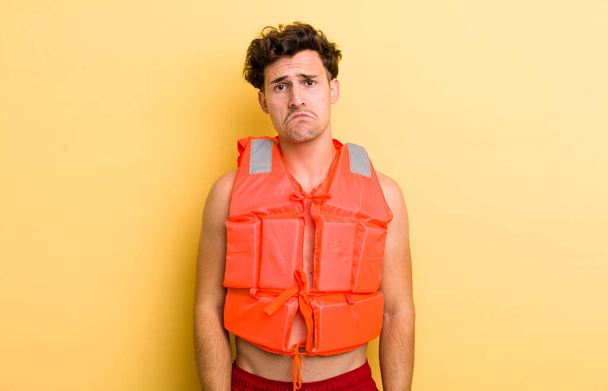 young handsome guy feeling sad and whiney with an unhappy look and crying. life jacket and boat concept - Fotografie, Obrázek
