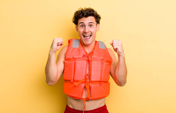 young handsome guy feeling shocked,laughing and celebrating success. life jacket and boat concept - Foto, imagen