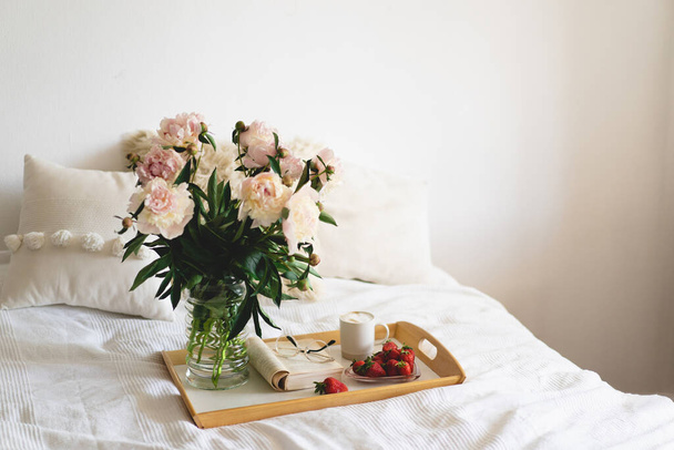 Still life details in home interior of living room. Open book with glasses, cup coffee, strawberries and bouquet white pink peonies flowers. Read and rest. Cozy home - Photo, Image