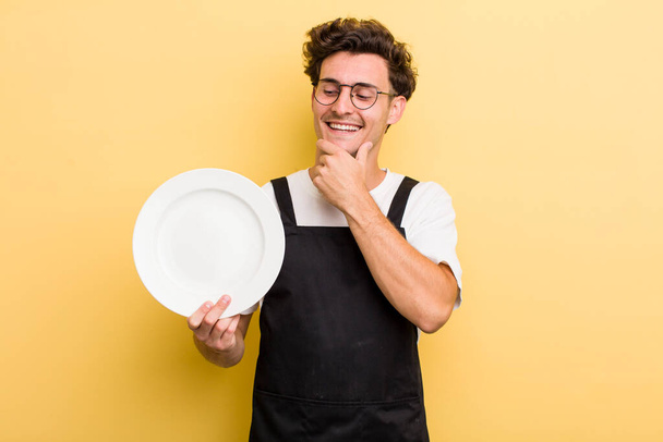 young handsome guy smiling with a happy, confident expression with hand on chin. empty dish concept - Photo, Image