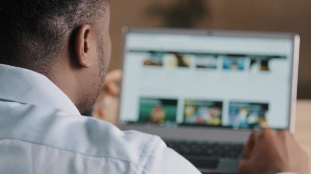 Over schouder weergave van mannelijke onherkenbare Afrikaanse man Amerikaanse jonge webdesigner programmeur freelancer kijken naar laptop scherm ontwikkelen online project scroll internet website pagina koos moderne interface - Video
