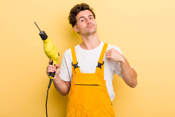 young handsome guy looking arrogant, successful, positive and proud. handyman with a drill concept - Photo, Image