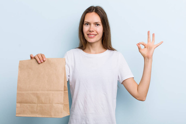 young adult woman feeling happy, showing approval with okay gesture. delivery and take away concept - Foto, afbeelding