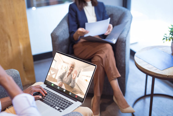 Midsection of african american businesswoman video conferencing with senior colleague over laptop. unaltered, wireless technology, teamwork, meeting, discussion, business, occupation and office. - Photo, image