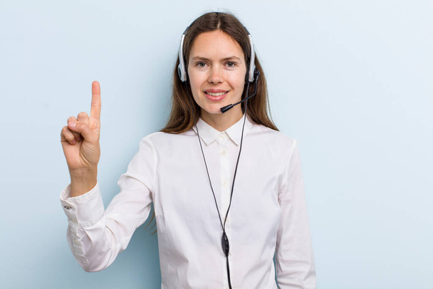 young adult woman smiling and looking friendly, showing number one. telemarketer concept - Zdjęcie, obraz