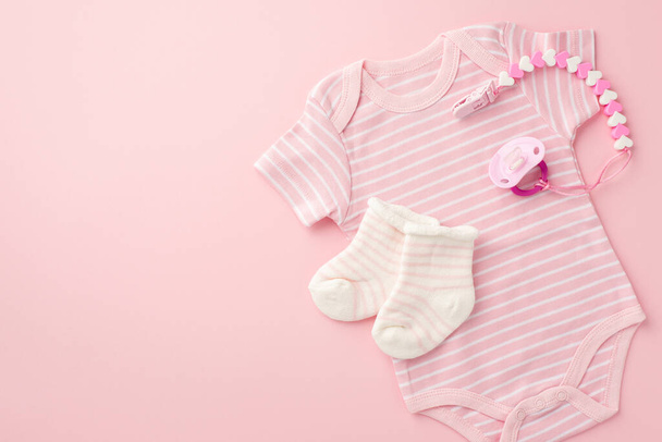 ベビーアクセサリーのコンセプト。ピンクの幼児服のボディスーツの靴下とペースメーカーチェーンのトップビューの写真孤立したパステルピンクの背景 - 写真・画像