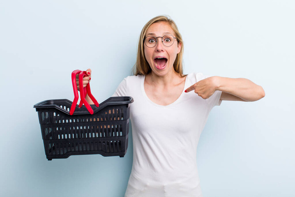 blonde young adult woman feeling happy and pointing to self with an excited. shopping basket - Photo, image