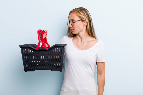 blonde young adult woman feeling sad, upset or angry and looking to the side. shopping basket - Photo, Image