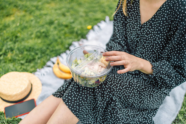 健康的なサラダと緑の自然を背景にエコ木製のフォークでボウルを保持幸せな女性。ピクニック中のきれいな女の子。食の概念 - 写真・画像