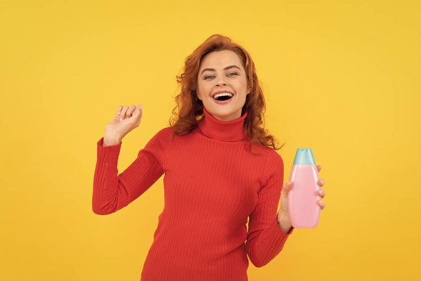 Kıvırcık saçlı mutlu kadın şampuan şişesinin vücut bakımıyla eğleniyor, kepek önleyici.. - Fotoğraf, Görsel
