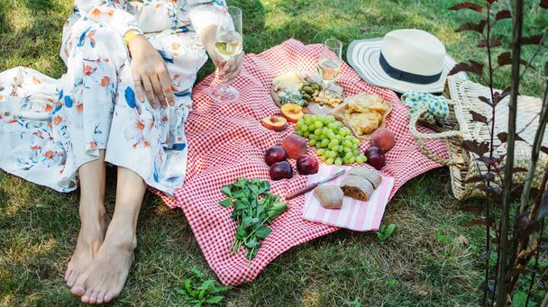 Przycięte zdjęcie dziewczyny siedzącej na trawie na łonie natury. Koncepcja pikniku w parku miejskim w letnie weekendy. - Zdjęcie, obraz