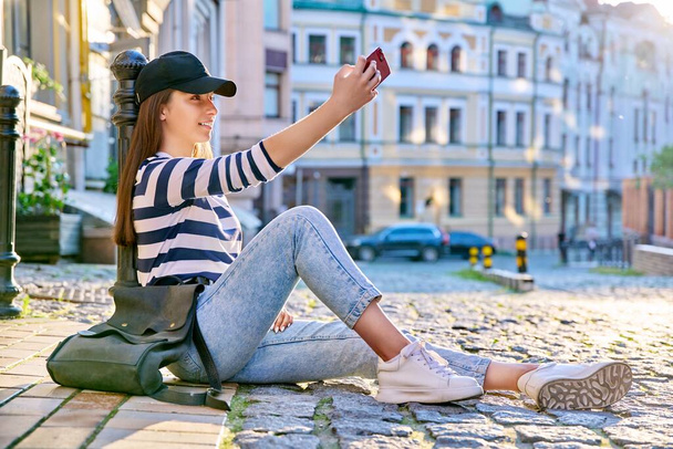 Urban style, fashionable teenage female sitting on the sidewalk using smartphone. Fashion, leisure, lifestyle, summer, beauty, youth concept - Foto, Bild