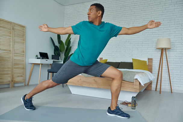 Handsome young multiracial man in sports clothing doing stretching exercise at home - Foto, immagini