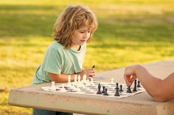 παιδί γιος παίζει σκάκι στο τραπέζι στο πάρκο υπαίθρια με τον πατέρα του, παιδική ηλικία. - Φωτογραφία, εικόνα