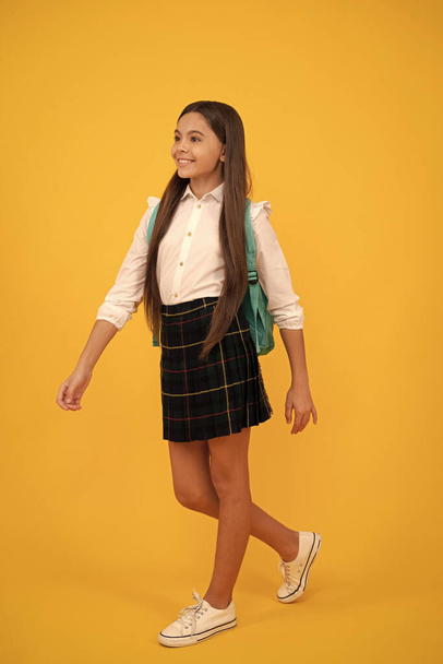 heureux adolescent fille avec sac à dos en uniforme scolaire pleine longueur sur fond jaune faire un pas en avant, école. - Photo, image