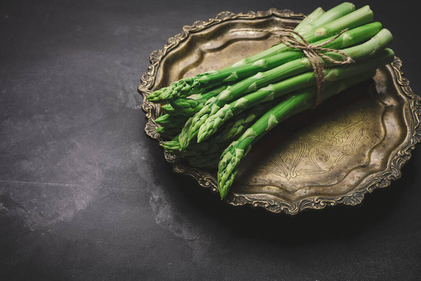 fresh green asparagus sprouts on a round copper plate, black background. View from above - Fotó, kép