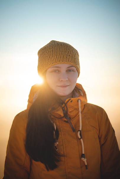 Utazó kellemes mosollyal, jellegzetes sárga kabátban áll egy hegy tetején a lengyel Beszkidek-hegységben naplementekor, élvezve a pillanatot. Valódi emberek télen jég környezetben. - Fotó, kép