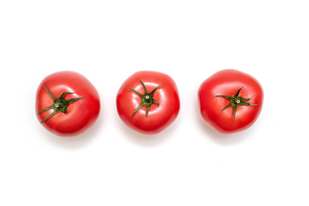 Three fresh tomatoes on a white isolated background. Fresh juicy tomatoes with green stems ready to eat or ingredient for cooking. Three tomatoes in a row top view - Φωτογραφία, εικόνα
