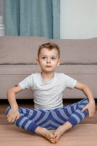 A gyerek lótusz pózol és együtt mosolyog. Mosolygó kisfiú portréja a jóga meditáción. Gyermek és jóga. - Fotó, kép