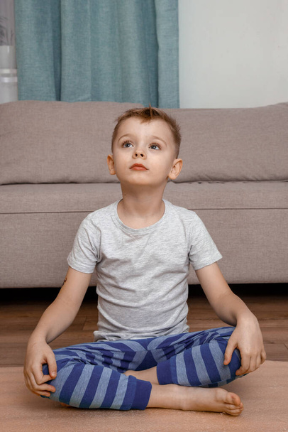 Child doing lotus pose and smiling together. Portrait of smiling boy child on yoga meditation session. Child and yoga. - 写真・画像