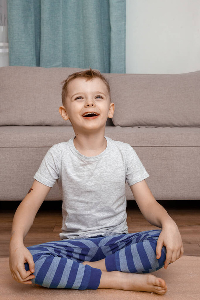 Kind doet lotuspose en glimlacht samen. Portret van een lachend jongetje op yoga meditatie sessie. Kind en yoga. - Foto, afbeelding