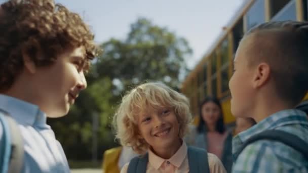 Drie scholieren lachen om de gele bus. Basisleeftijd jongens wachten op schoolbus boarding close-up. Leuke glimlachende leerlingen met rugzakken die samen plezier hebben in de buurt van het voertuig. Onderwijsconcept. - Video
