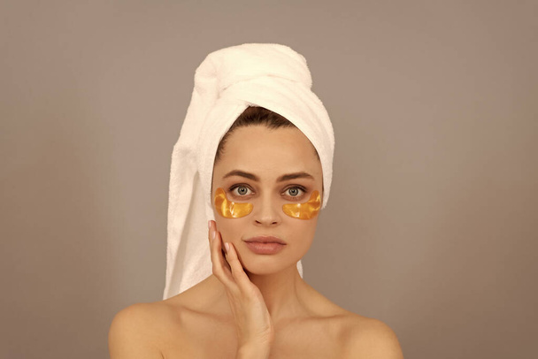 молодая женщина с махровым полотенцем использовать лицо золотая повязка для кожи, кожа. - Фото, изображение