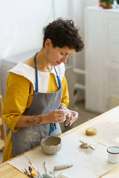 若い陶芸家は、粘土を形成するための専門的なツールを使用して手作りのセラミックポットマグカップの成形に焦点を当てました。女性の職人は創造的なスタジオワークショップスペースで一人で働く。手芸業 - 写真・画像