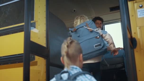 Multiethnische Kinder steigen in einen gelben Schulbus ein. Konzentrierte Autofahrer kontrollieren Schüler. Energetische Schüler im Grundschulalter, die im Shuttle nach oben fahren. Öffentliches Bildungskonzept. - Filmmaterial, Video