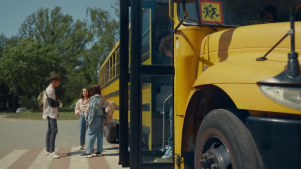 Due bambini che escono dallo scuolabus. Adolescenti gioiosi in piedi al bus accademico a parlare. Tre amici che posano alla luce del sole. Ragazzi con lo zaino che lasciano la navetta gialla. Concetto di studio - Filmati, video