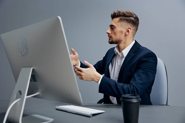 guapo hombre de negocios cansado vaso de café trabaja en frente de un fondo gris ordenador. Foto de alta calidad - Foto, Imagen