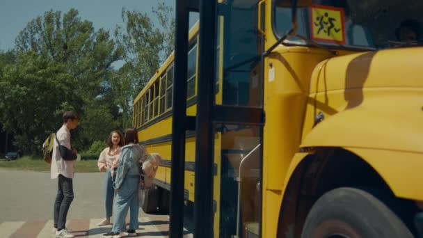 Two preteen classmates leaving yellow school bus open door. Focused serious pupils going out academic shuttle. Diverse cheerful teenagers standing talking together near children vehicle transport. - Footage, Video