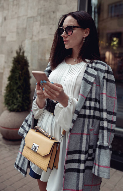 Beautiful stylish female in sunglasses texting on smartphone at street. City life. Business lady. - Foto, Bild