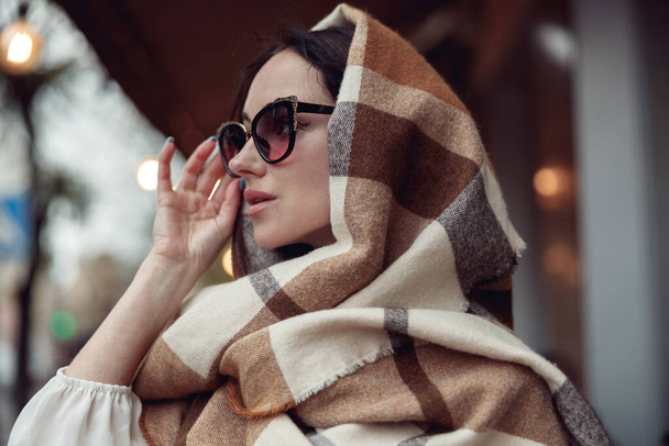 Primo piano di attraente giovane donna con occhiali da sole scuri e sciarpa variopinta sulla testa in città. Ritratto. - Foto, immagini