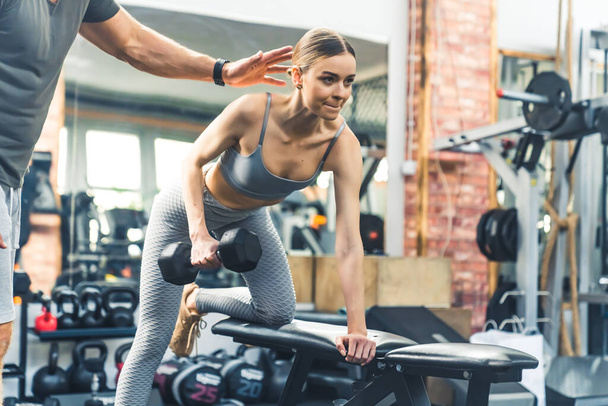 Healthy lifestyle concept. Physical exercises. Confident European young adult woman exercising for the triceps weights over bench under the guidance of her personal trainer. High quality photo - Foto, afbeelding