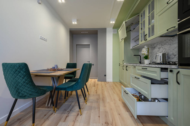 Modern trend açık yeşil lüks mutfak, yemek masası ve koyu yeşil sandalyeler, bazı çekmeceler geri çekilir - Fotoğraf, Görsel
