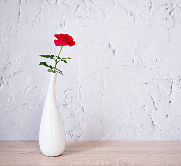 Red rose in white vase on wood table beautiful green leaf copy space for text or lettering flower in ceramic on wooden table ,texture cement background or wallpaper ,creative celebrating card  - Zdjęcie, obraz
