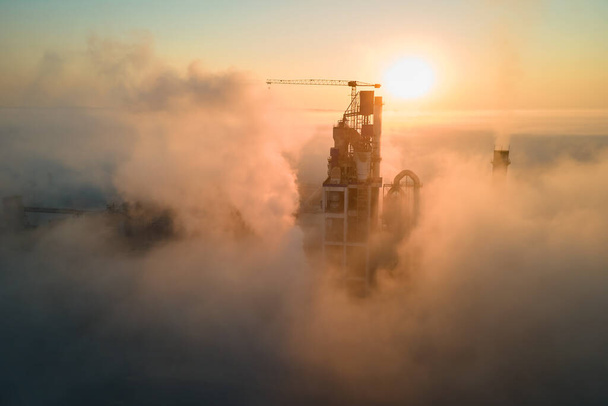 Luftaufnahme einer Zementfabrik mit hoher Betonwerkstruktur und Turmdrehkran an einem nebligen Abend. Produktion und globales Branchenkonzept. - Foto, Bild